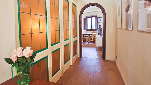 Un pasillo con piso de madera, puertas con marco verde y techo de madera con detalles decorativos.