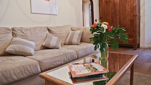 Un salón con un sofá color crema, una mesa de centro con un libro y un jarrón con flores.