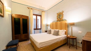 Un dormitorio con cama, mesitas de noche, armario y ventana con cortinas.
