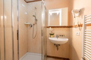 A modern bathroom with a glass-enclosed shower, a white sink with a gold-colored planter, and a hairdryer mounted on the wall. - Sprone (Florence)
