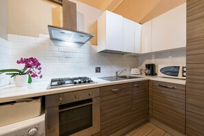 A modern kitchen with white cabinets, a stainless steel range hood, a microwave, a sink, and a stove. - Sprone (Florence)
