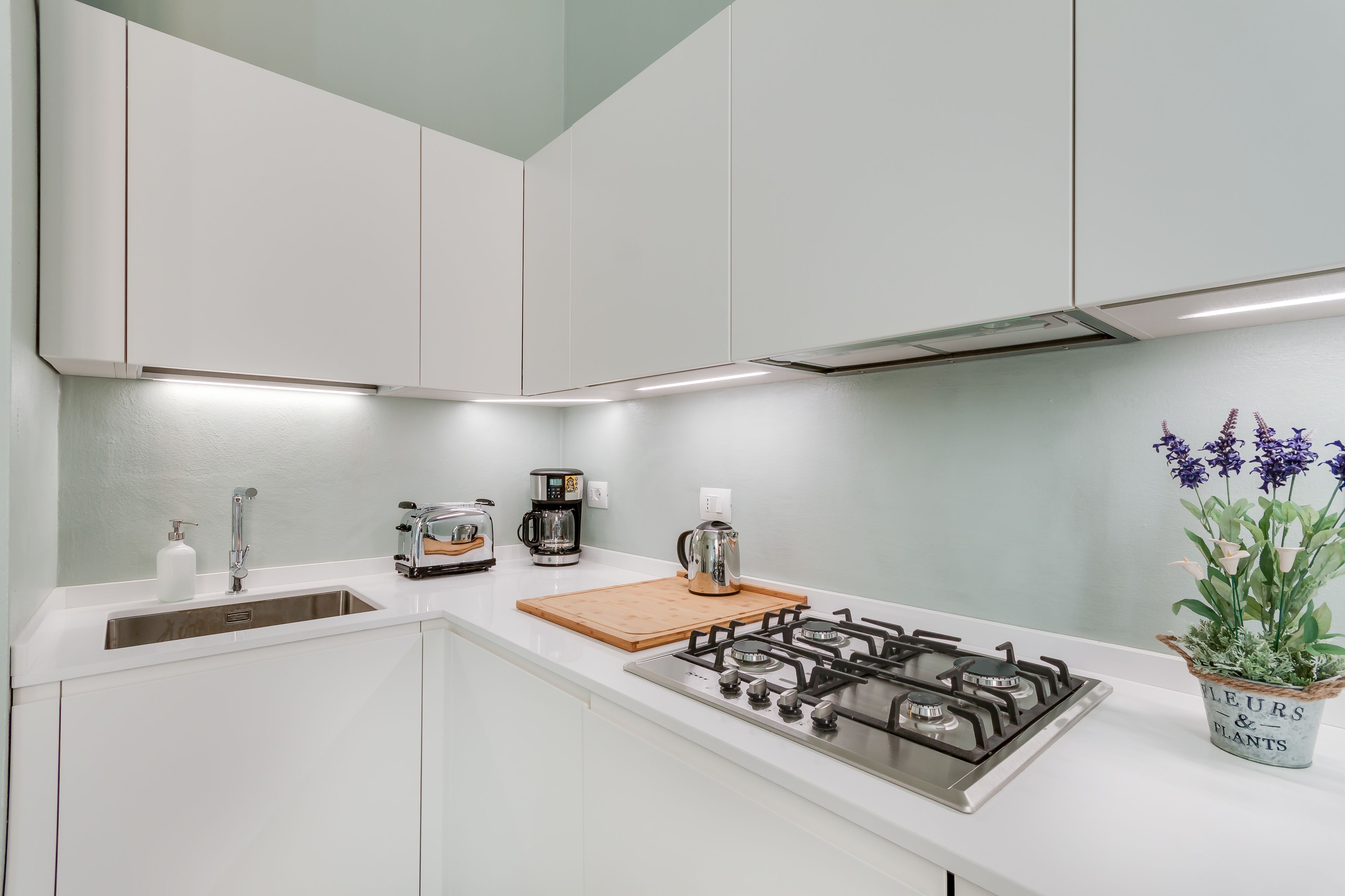 A modern kitchen with white cabinets, a gas stove, a coffee maker, and a wooden cutting board.