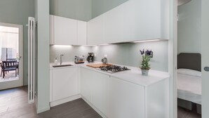 Een kleine keuken met witte kastjes, een gasfornuis, een koffiezetapparaat en een potplant.