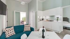 Een moderne woonkamer met een blauwgroene bank, een eettafel met wijnglazen, en een keuken met witte kasten.
