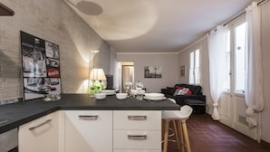 Een moderne keuken met witte kasten, een zwart aanrecht en een eethoek met een zwarte bank en een witte stoel.