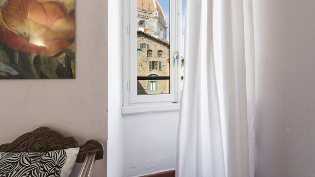 Een kamer met een bed, een raam met uitzicht op een gebouw met een koepel, en een schilderij aan de muur.
