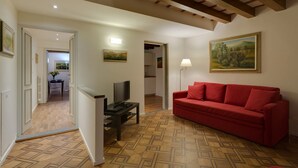 Una sala de estar con un sofá rojo, un televisor sobre un mueble, una lámpara y un cuadro en la pared.