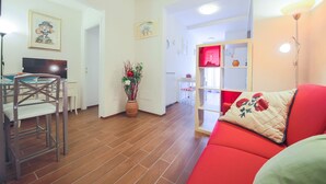 Una sala de estar con un sofá rojo, una zona de comedor con televisor y una cocina con un armario rojo.