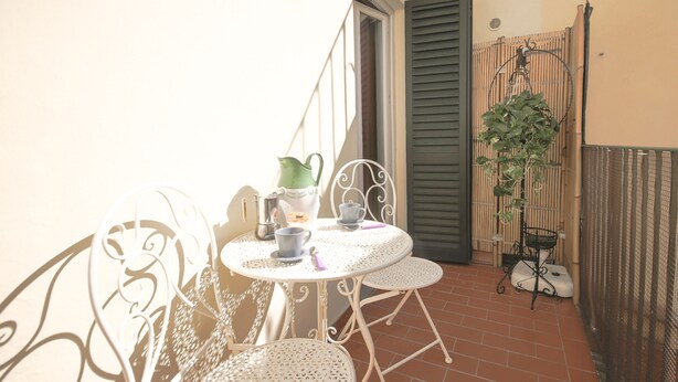 Un pequeño patio al aire libre con una mesa redonda y dos sillas, una jarra verde y una taza.