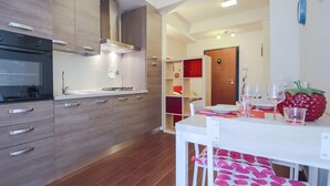 Una cocina moderna con armarios de madera, horno integrado y comedor con mesa y sillas blancas.