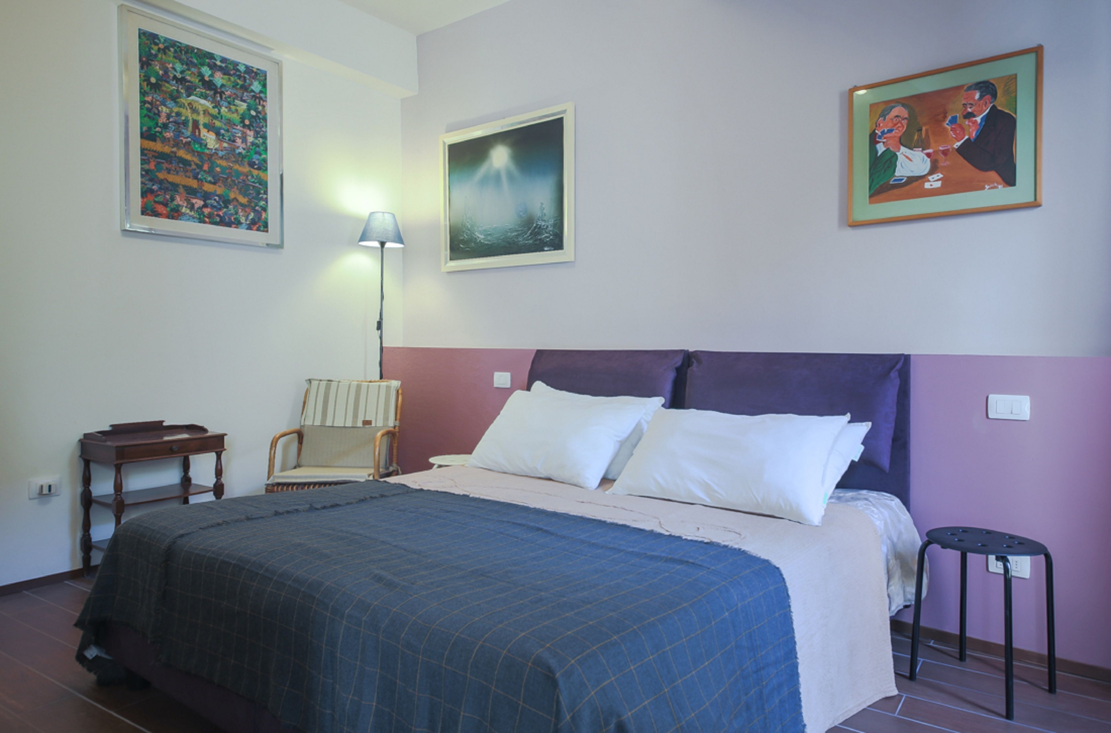 Un dormitorio con cama, una silla, una mesita de noche y una lámpara.