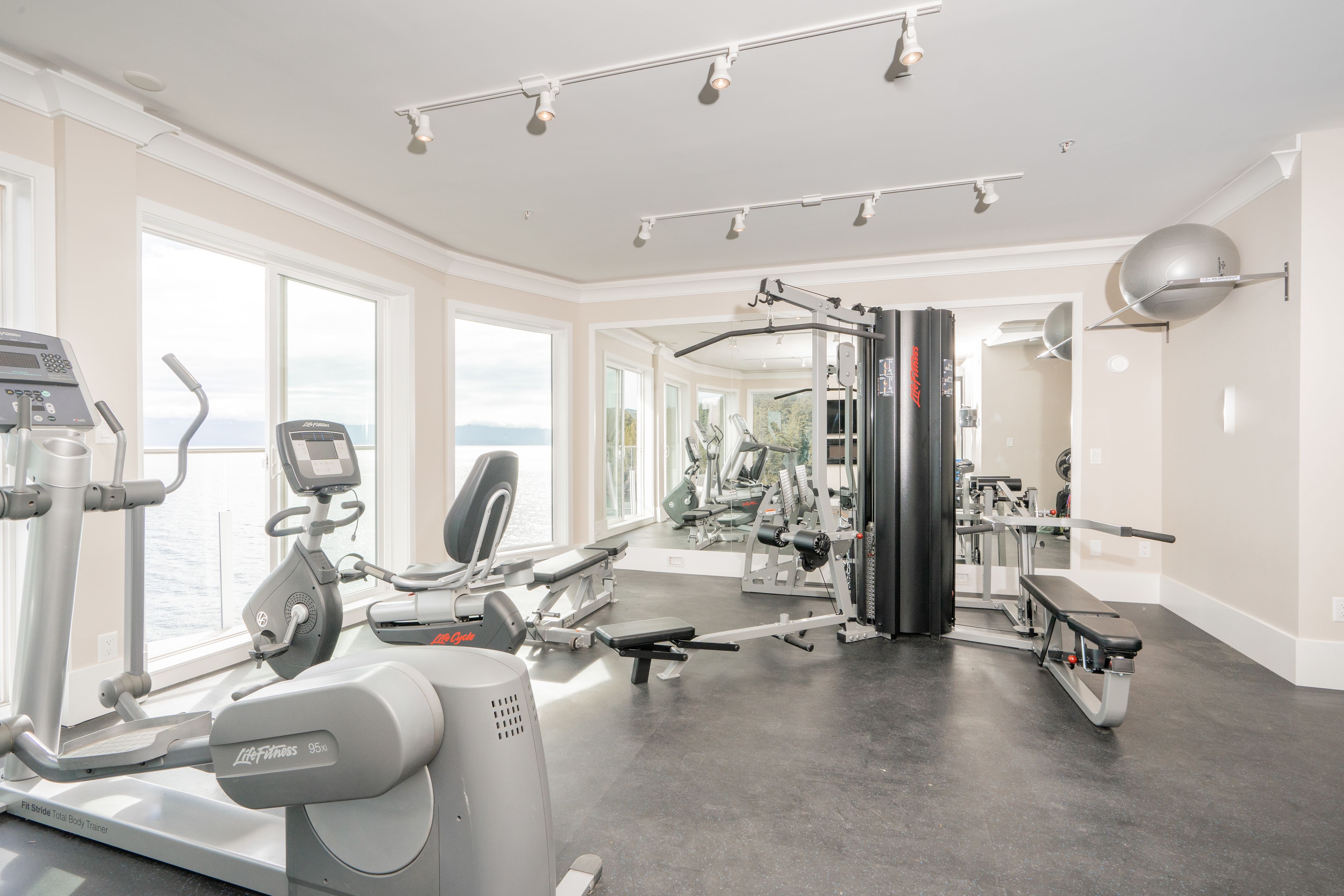 Ein Fitnessstudio mit Cardiogeräten, Krafttrainingsgeräten und großen Fenstern mit Blick ins Freie.