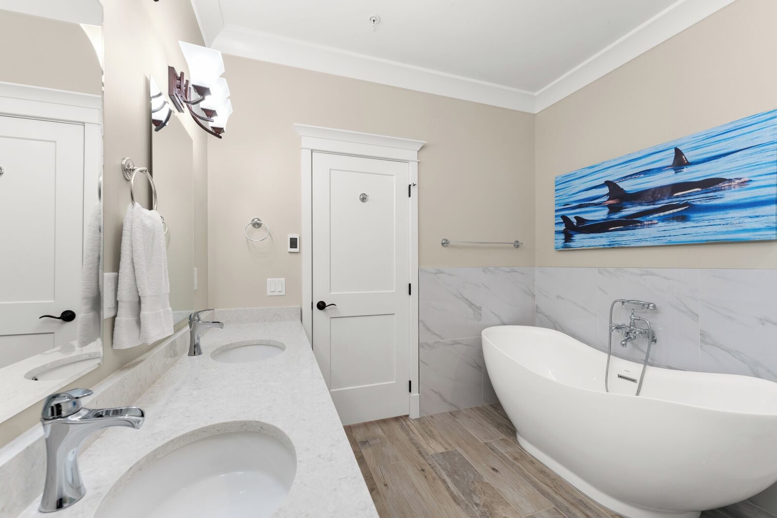 A modern bathroom with two sinks, a large bathtub, and a painting of sharks on the wall.