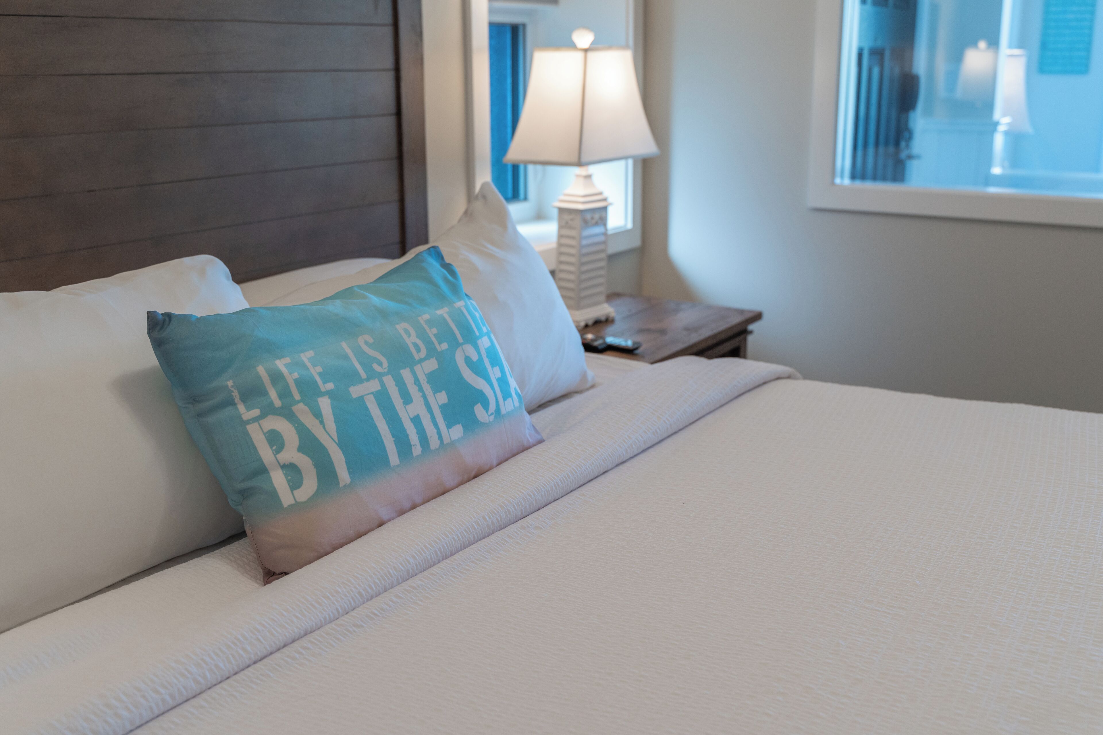 A neatly made bed with a pillow that reads "Life is better by the sea."