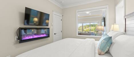 A hotel room with a large bed, a mounted TV, a window with a view of greenery, and a wall-mounted aquarium.