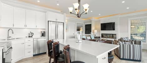 Una cocina moderna con armarios blancos, electrodomésticos de acero inoxidable y una isla central con taburetes de bar.