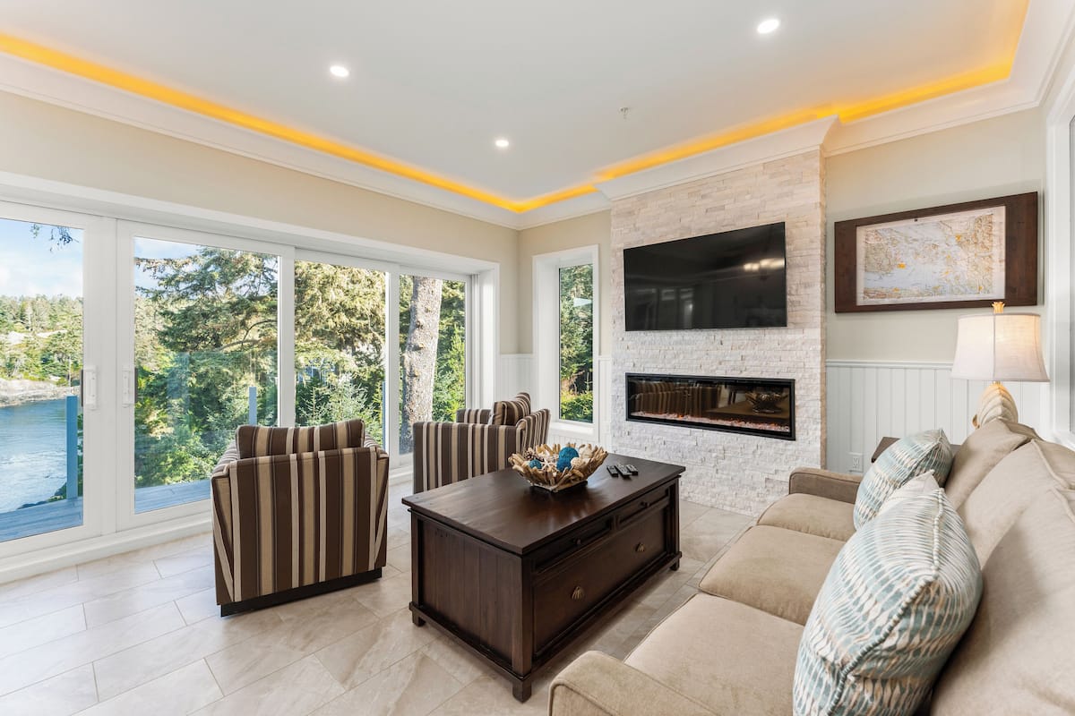 A modern living room with a fireplace, large windows, and a view of the outdoors.