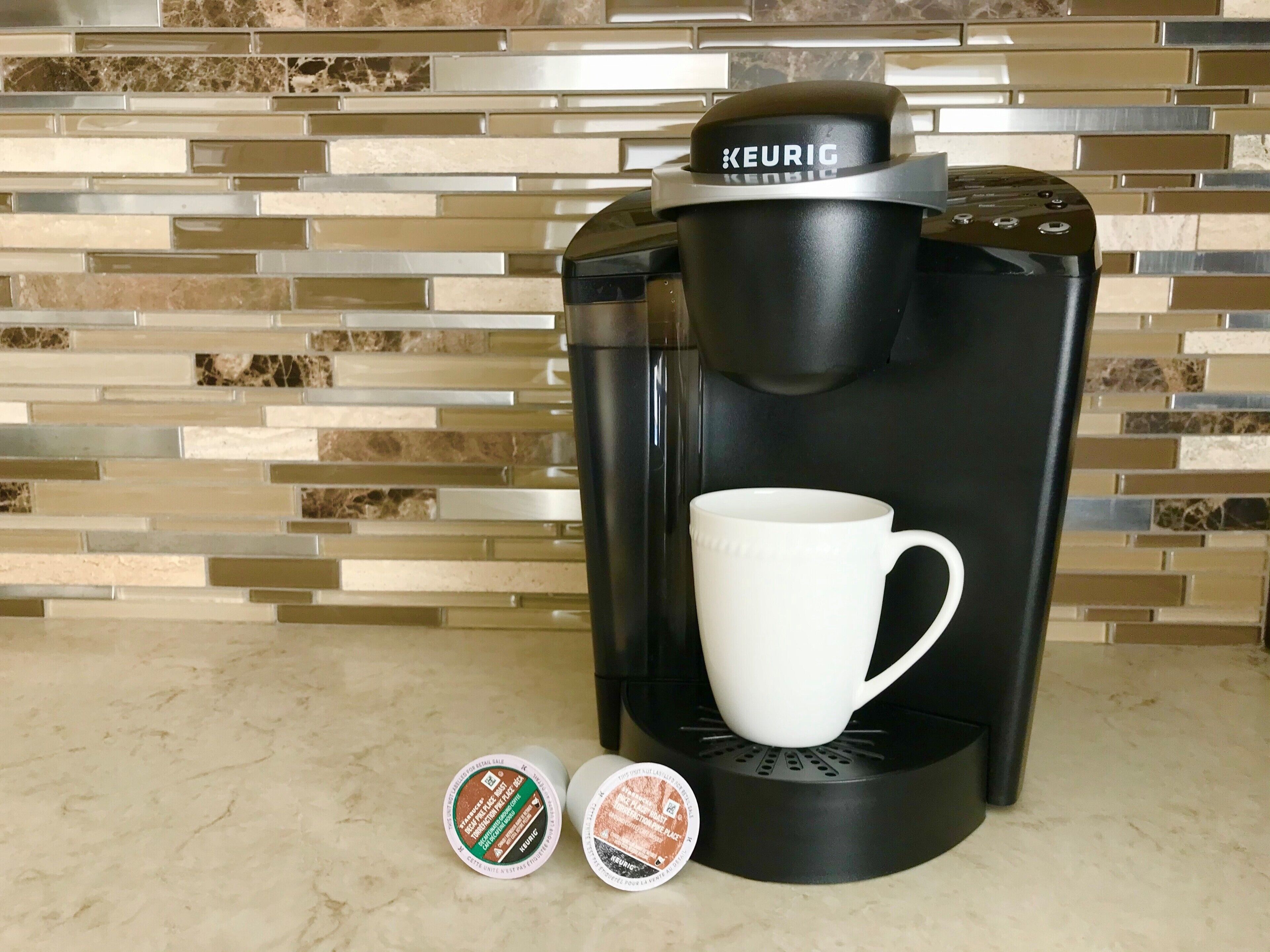 A Keurig coffee maker with a white mug and two coffee pods on a countertop.