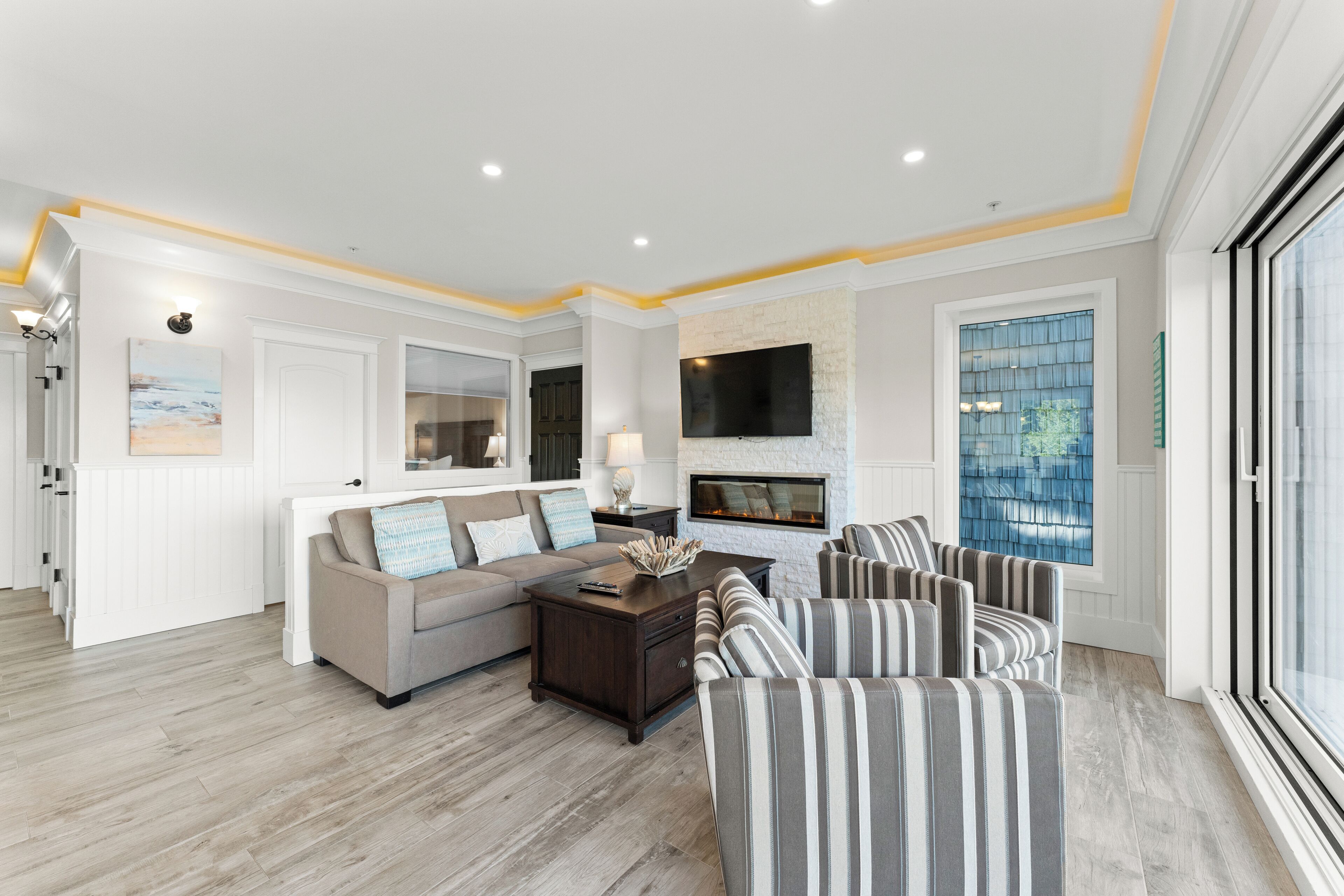 A modern living room with a fireplace, a sofa, striped chairs, and a large window.