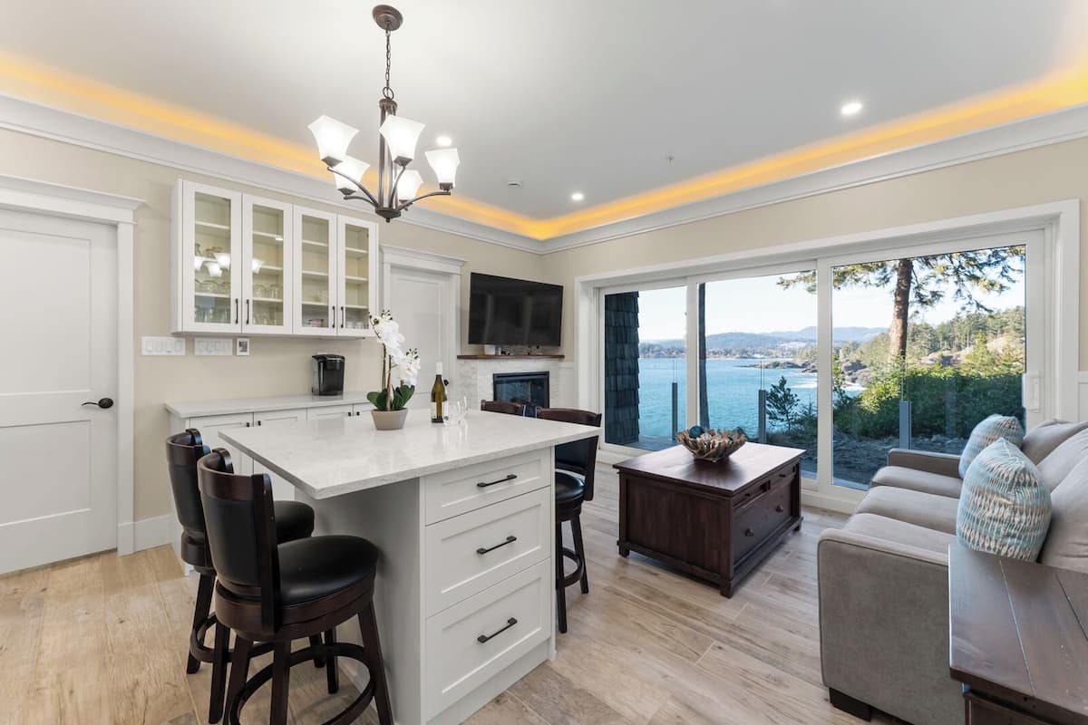 A modern kitchen with a central island, white cabinetry, and a large window overlooking a scenic landscape.