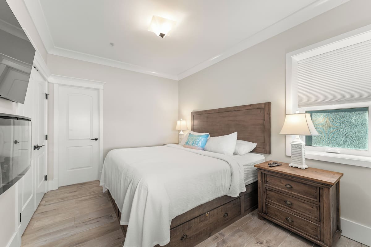 A bedroom with a bed, bedside tables, a dresser, a window with blinds, and a ceiling light.