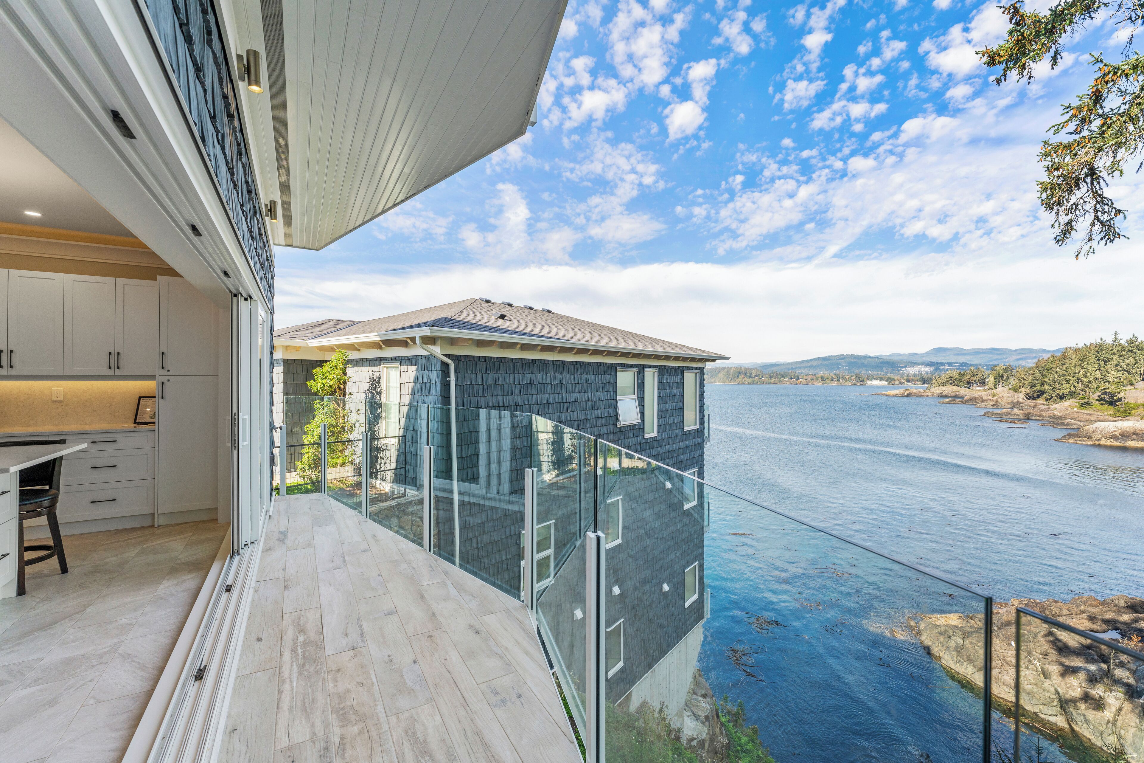 Une maison moderne dotée d’un balcon en verre donnant sur une rivière.