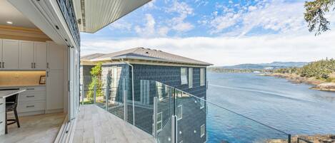 Une maison moderne dotée d’un balcon en verre donnant sur une rivière.