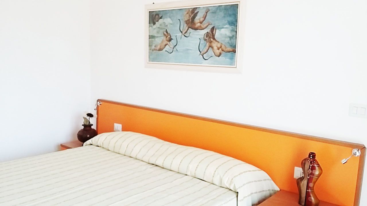 Een slaapkamer met een bed, een nachtkastje, een vaas en een schilderij aan de muur.