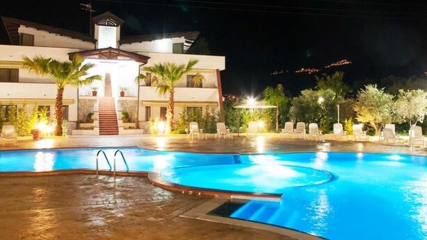 A swimming pool with a circular design, surrounded by lounge chairs and palm trees. - Suite Hotel Club Dominicus (Grisolia)