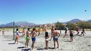 A group of people playing volleyball on a sandy beach with mountains in the background. - Suite Hotel Club Dominicus (Grisolia)