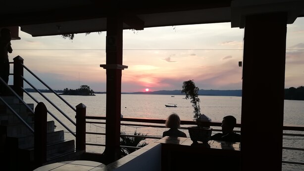 A terrace with a view of the sunset over a body of water, featuring a railing and a potted plant. - Hotel La Union (Flores)