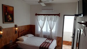 A hotel room with a bed, a ceiling fan, an air conditioner, a painting, and a window with curtains. - Hotel La Union (Flores)
