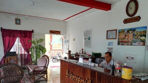 A hotel reception area with a wooden reception desk labeled "Bienvenidos," a clock, and various informational posters on the walls. - Hotel La Union (Flores)
