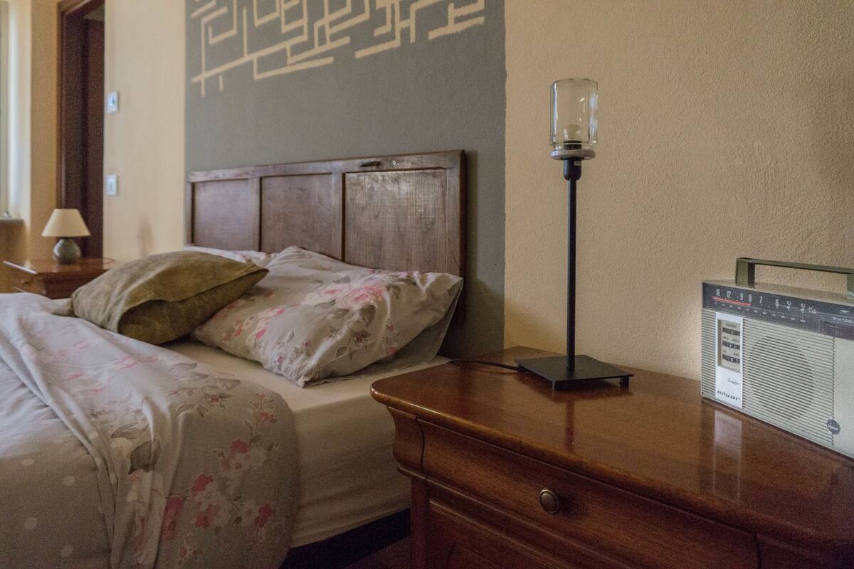 Un dormitorio con cabecera de madera, una mesita de noche con lámpara y un radio sobre un aparador.