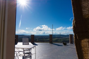 Eine Terrasse mit Tisch und Stühlen, Blick auf die Landschaft und ein klarer Himmel.