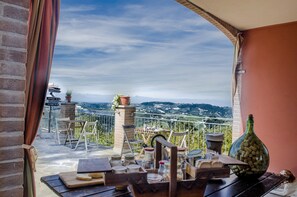 A balcony with a table set for dining, potted plants, and a view of distant hills. - B&B La Buonora (Sinio)