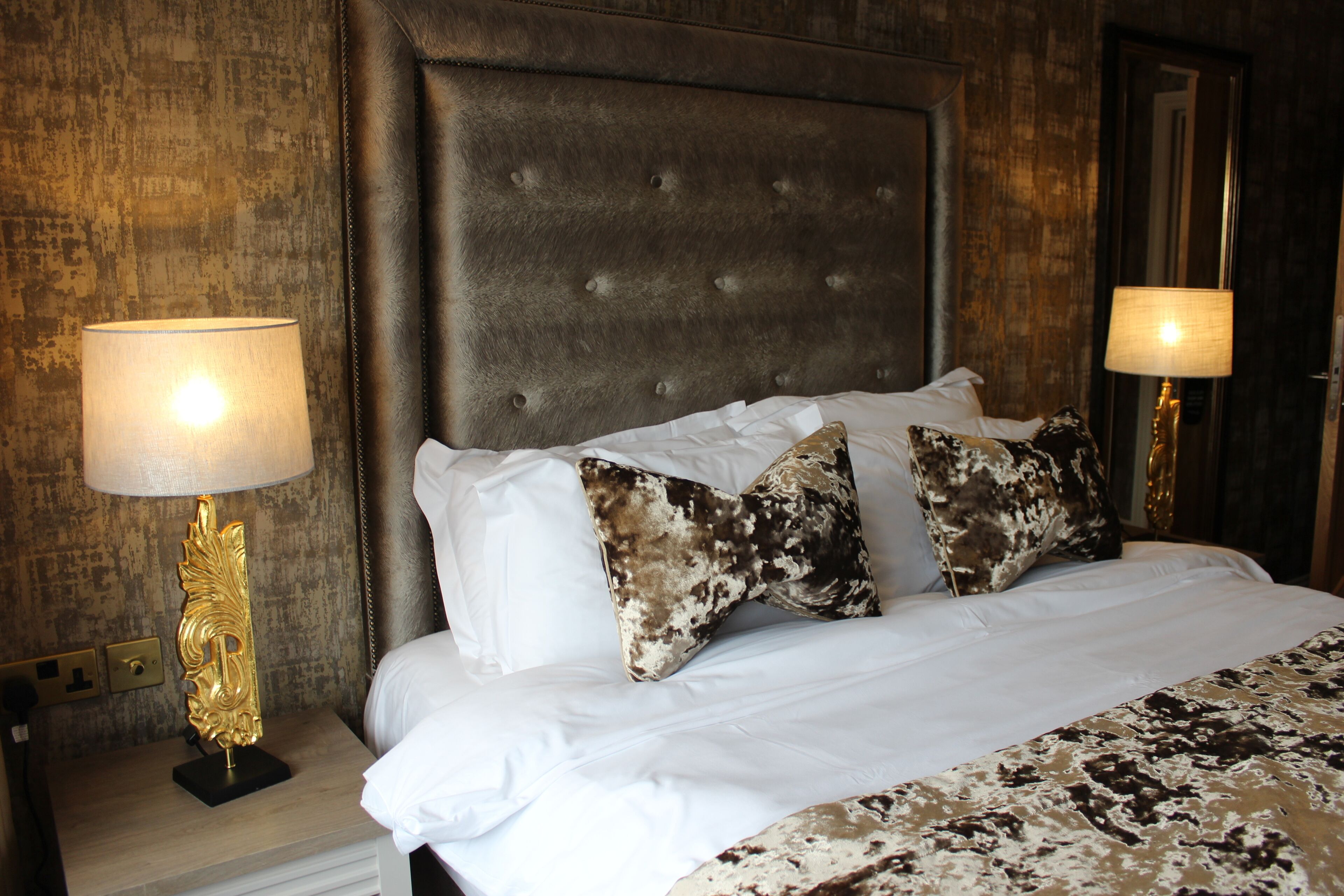 A neatly made bed with white linens and patterned pillows, flanked by two bedside lamps with gold bases.