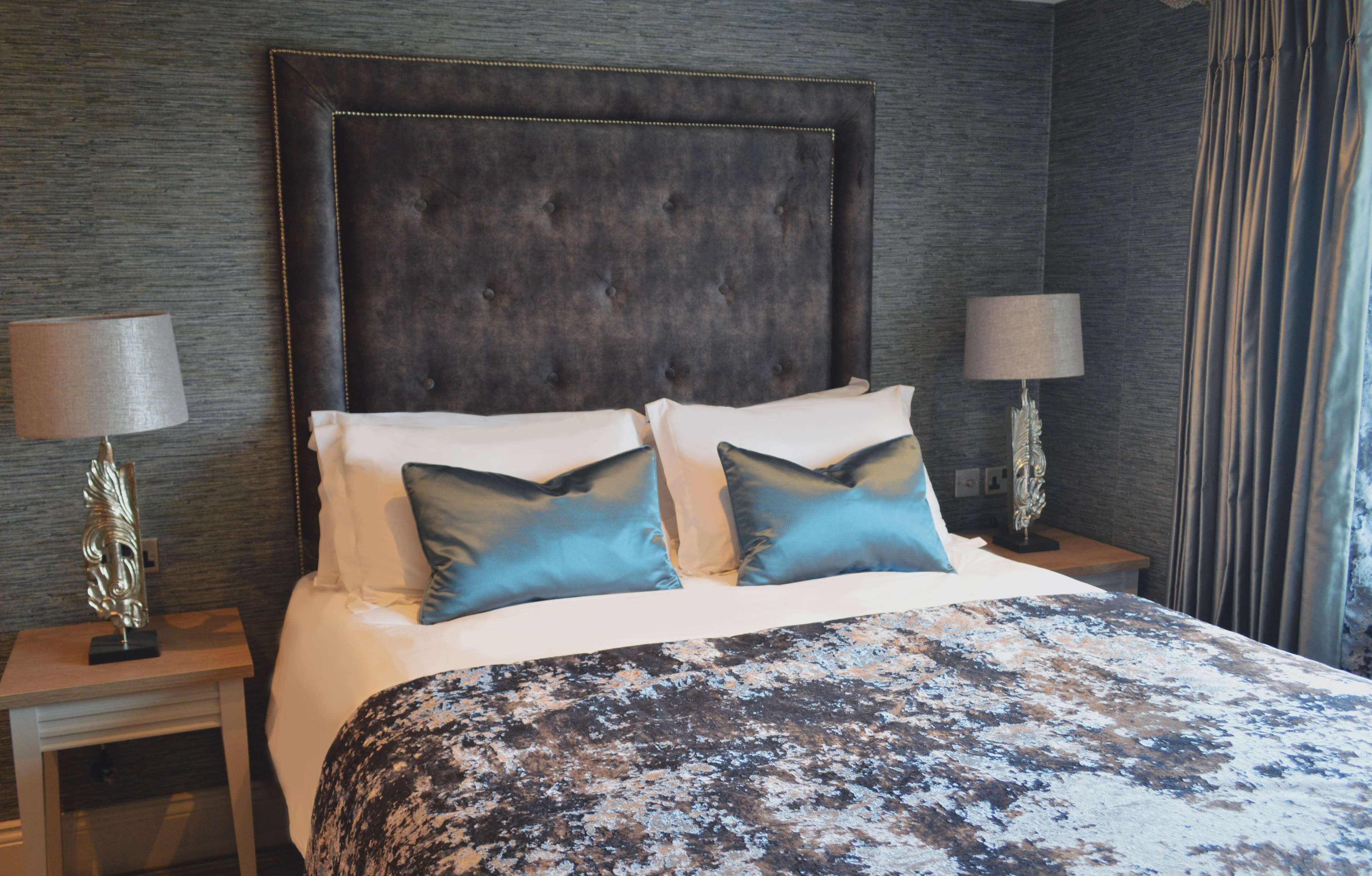 A hotel room with a large bed, two bedside tables with lamps, and a dark headboard.