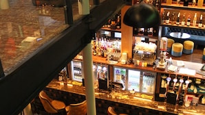 Et barområde med flere siddepladser, en bar med diverse flasker, og en trappe op til et højere niveau.