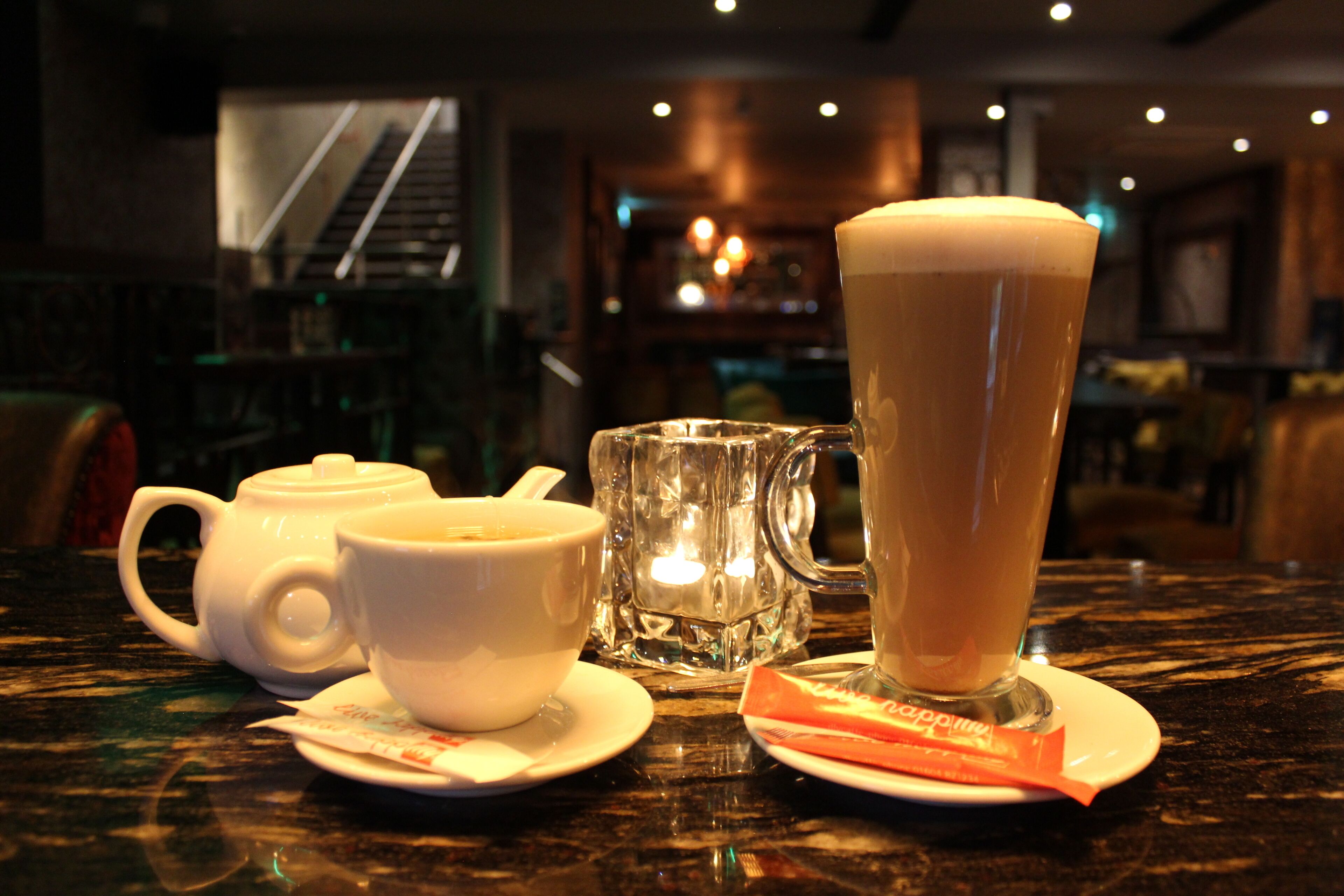A table with a teapot, a cup, a mug, and a packet of sugar.