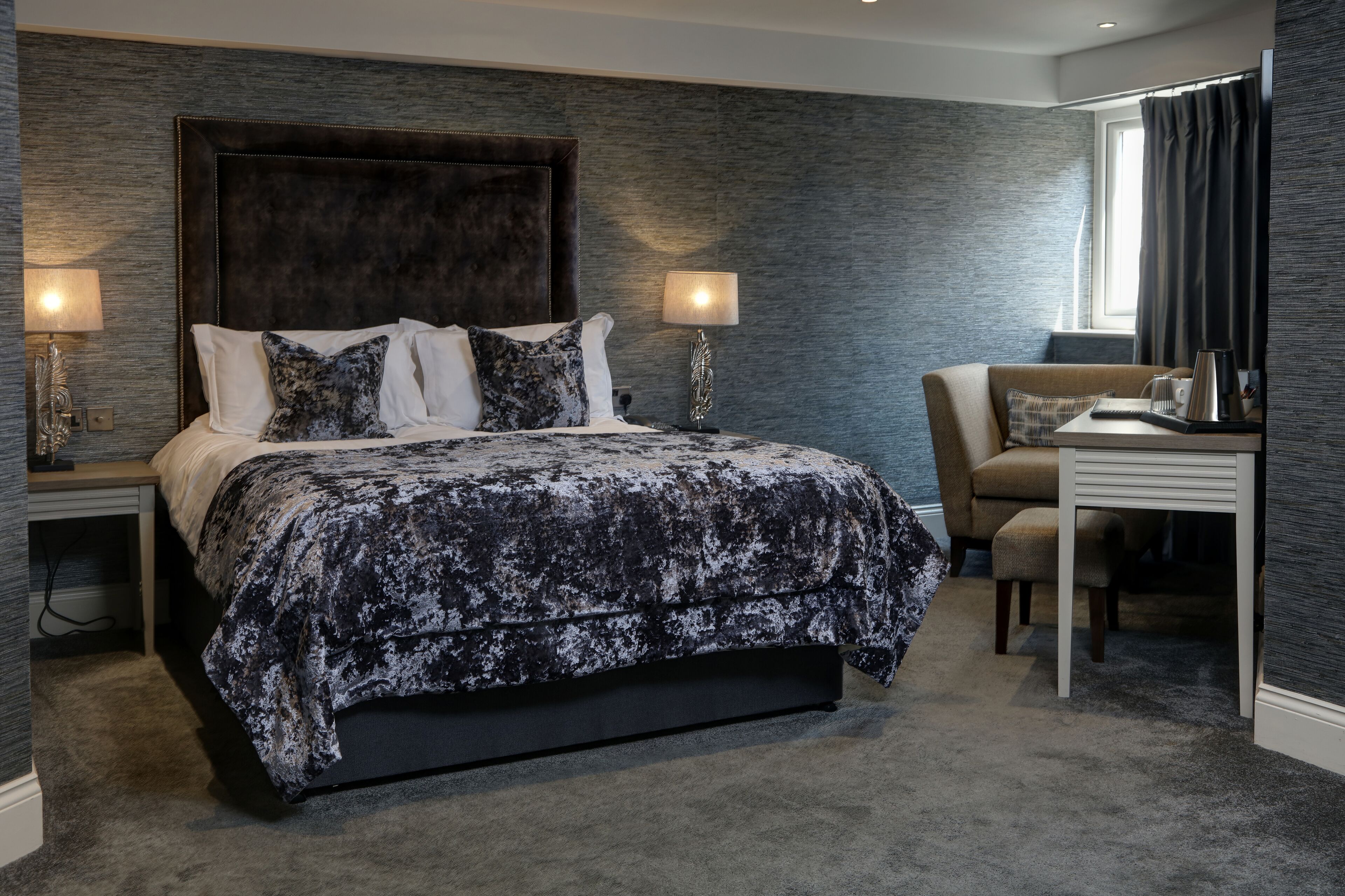 Ein modernes Schlafzimmer mit einem großen Bett, zwei Nachttischlampen, einem Sofa und einem Schreibtisch mit Kaffeemaschine.