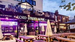 Et udendørs siddeområde med træborde og parasoller ved Lord Street Hotel.