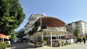 A restaurant with outdoor seating, a covered patio, and a signboard advertising food. - Sun Kiss Otel (Manavgat)