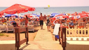 A beach with rows of sun loungers and umbrellas, a wooden walkway leading to the beach, and a clear view of the sea. - Sun Kiss Otel (Manavgat)