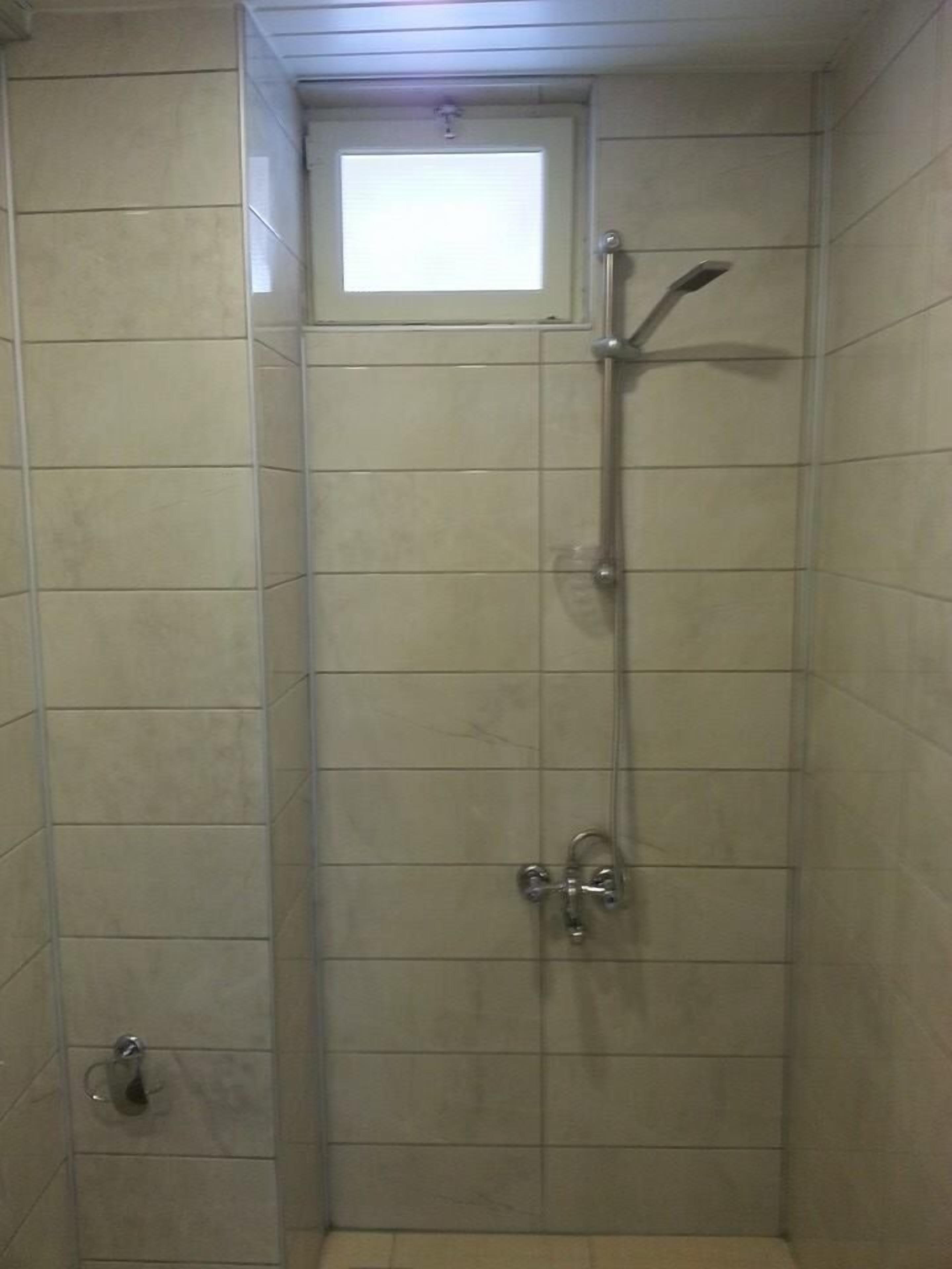 A small, tiled shower stall with a window above the door and a handheld showerhead.
