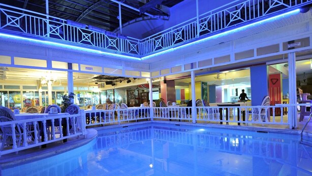 An indoor swimming pool with a white railing, surrounded by various shops and seating areas. - Sun Kiss Otel (Manavgat)