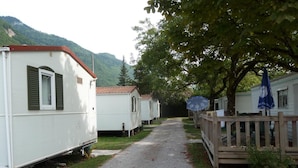 A row of white mobile homes with green shutters, a gravel path, and a wooden fence. - Camping le Lanfonnet (Talloires-Montmin)