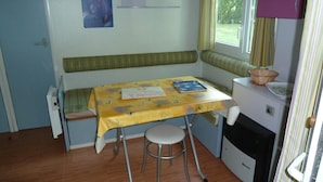 A compact room with a small table, a bench, and a window with curtains. - Camping le Lanfonnet (Talloires-Montmin)