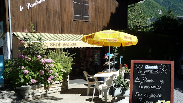 A storefront with a sign reading "SHOP WINKEL" and a yellow umbrella. There is a chalkboard menu with items like "Pains," "Viennoiseries," and "Boissons." - Camping le Lanfonnet (Talloires-Montmin)