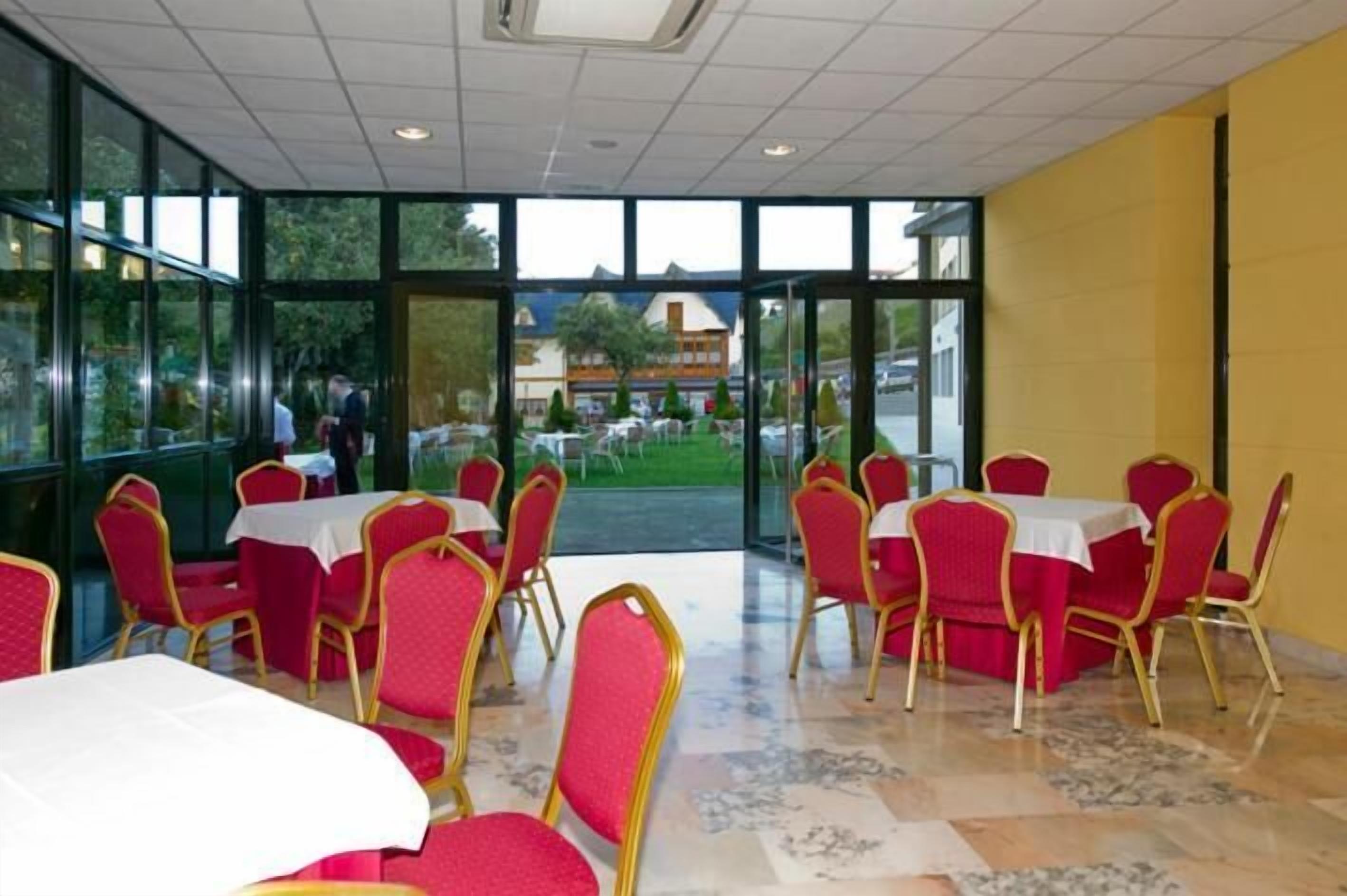 A dining area with tables and chairs, large windows, and a view of the outside.